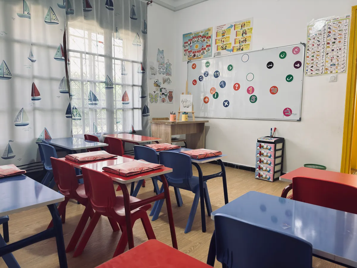 Blue and red tables with pencil cases, an emotions chart and sailboat curtains.