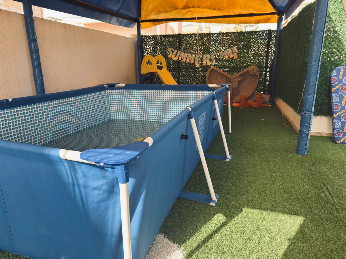 Above-ground pool under a covered shelter, on artificial grass.