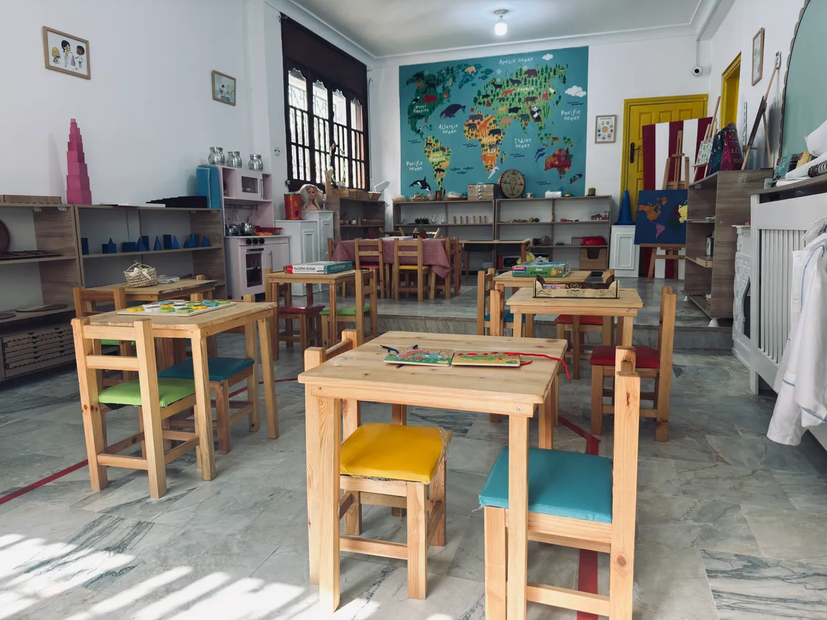 Small wooden tables with colourful seats, the Montessori pink tower and a world map in the background.