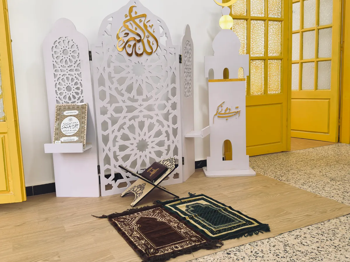 Corner set up with calligraphy panels, a small minaret, a book stand and prayer mats.