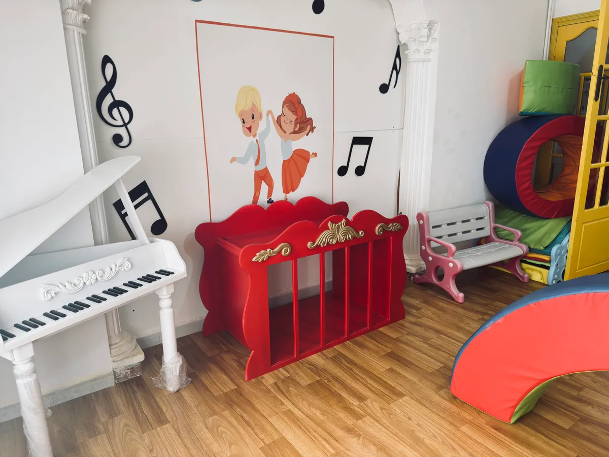 Music corner: a small white piano, a red cabinet and musical notes decorating the wall.