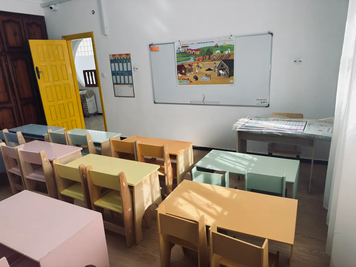 Classroom with small pastel desks, a yellow door and a whiteboard with a farm poster.