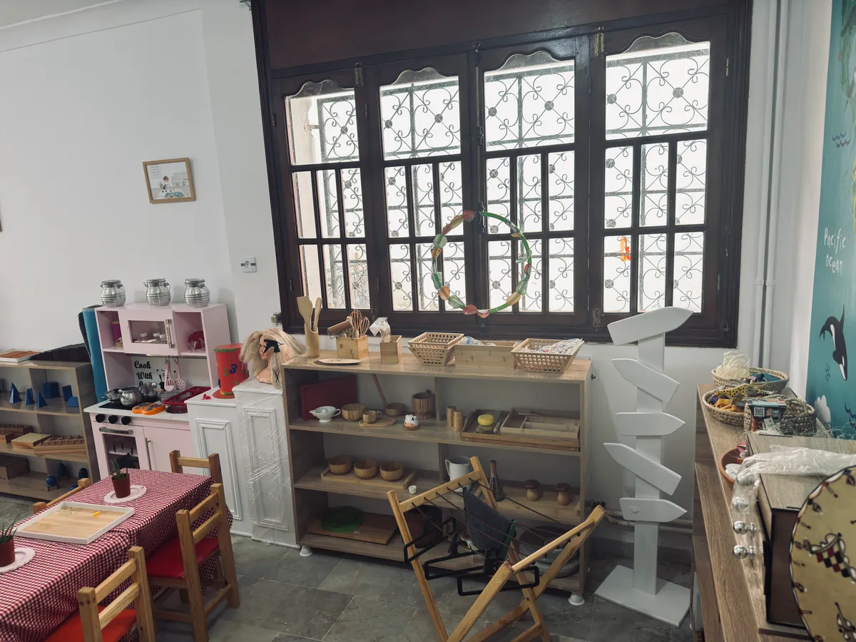 Wooden shelves under a large window, with baskets, trays and everyday objects at child height.
