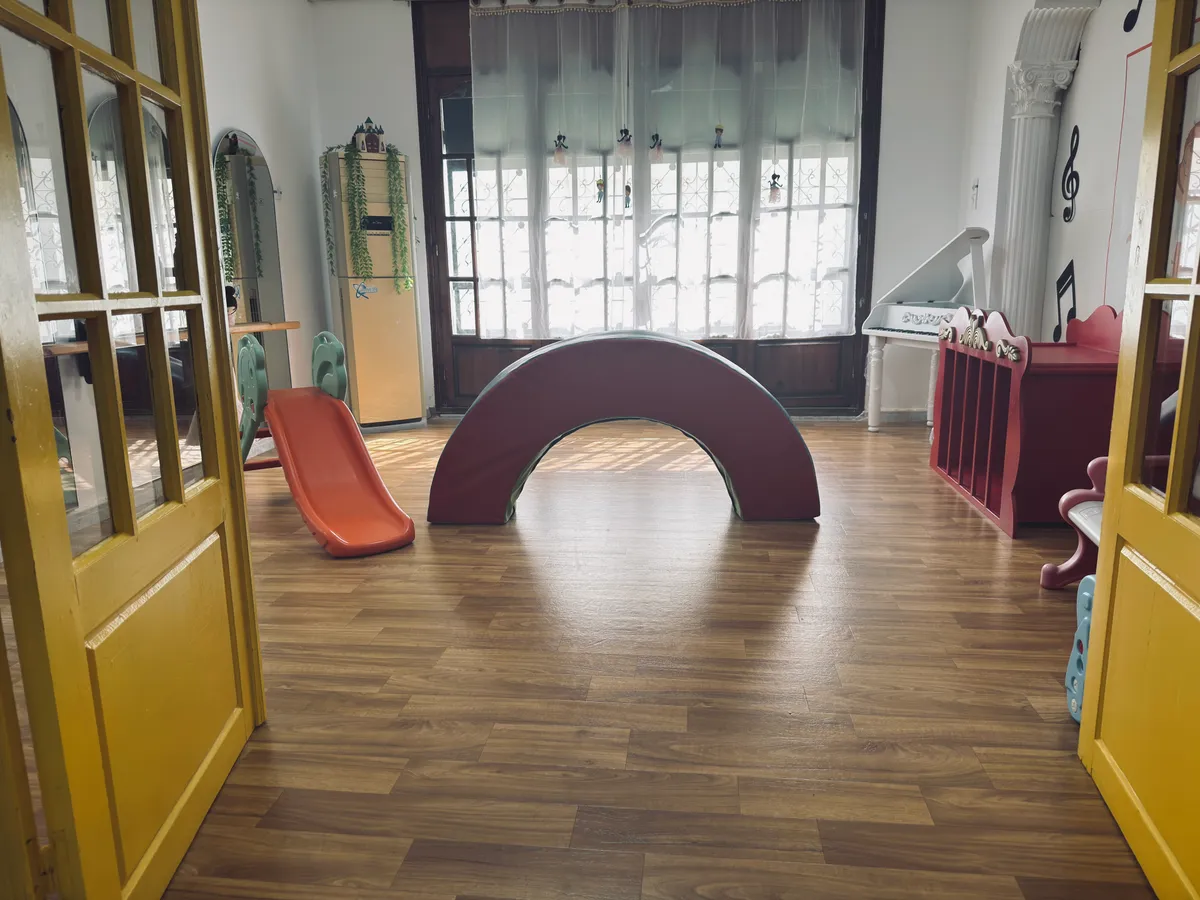 Movement room with a light wooden floor: a rocking arch, a small slide and large windows.