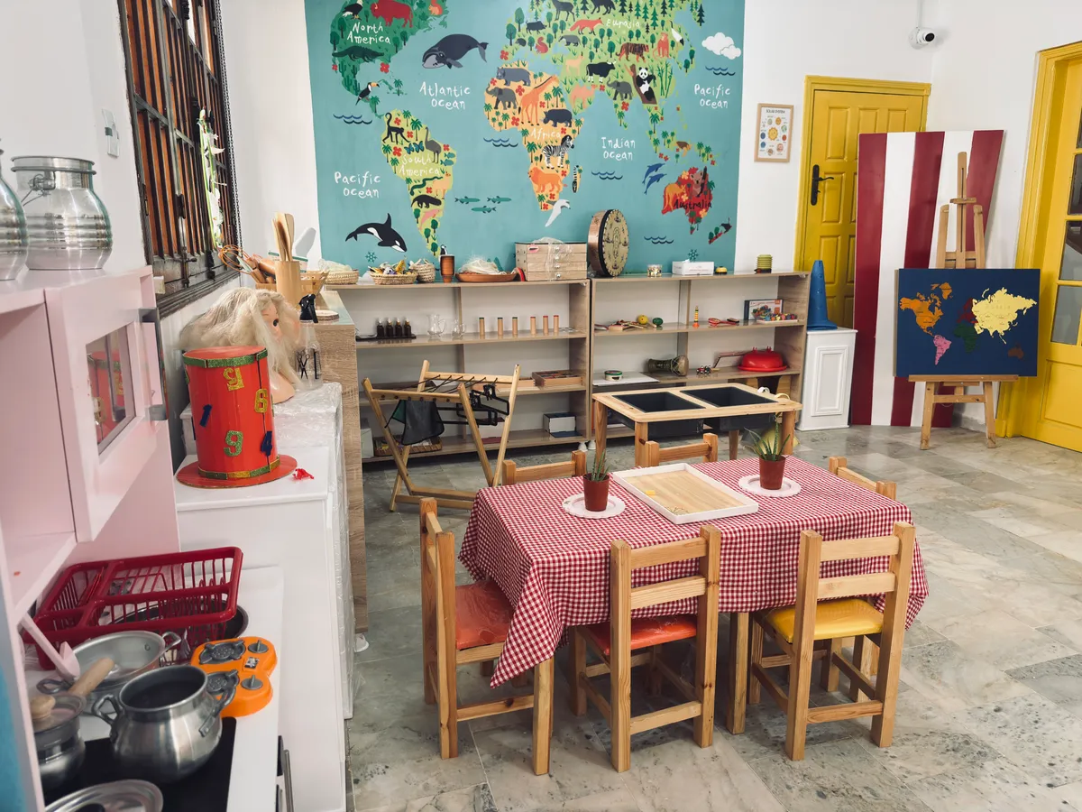 Montessori room: a gingham-covered table, a child-size play kitchen and a large world map on the wall.