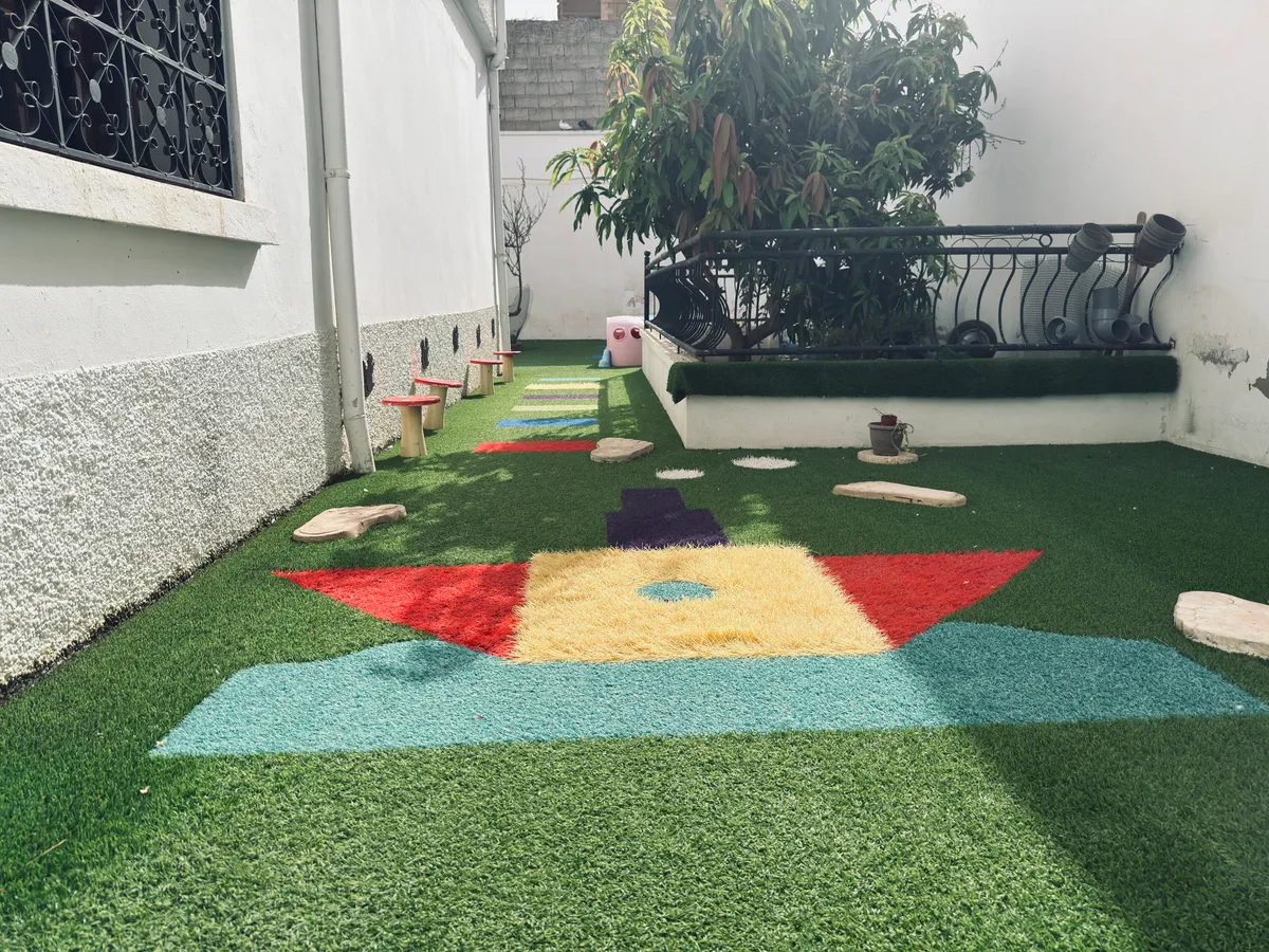 Garden with artificial grass: stepping stones, colourful shapes on the ground and plants.