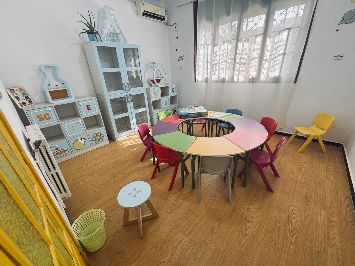 Science room: a multicoloured round table, light blue cabinets and a flask-shaped shelf.