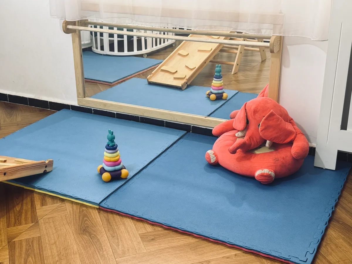 Play mat in front of a low mirror, with stacking rings and a large soft toy.