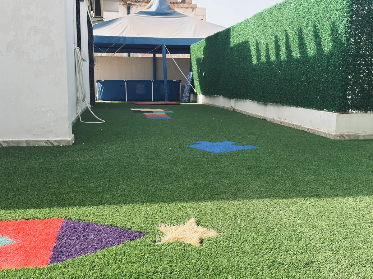 Sunny terrace with a star and colourful shapes on the ground and a green hedge.