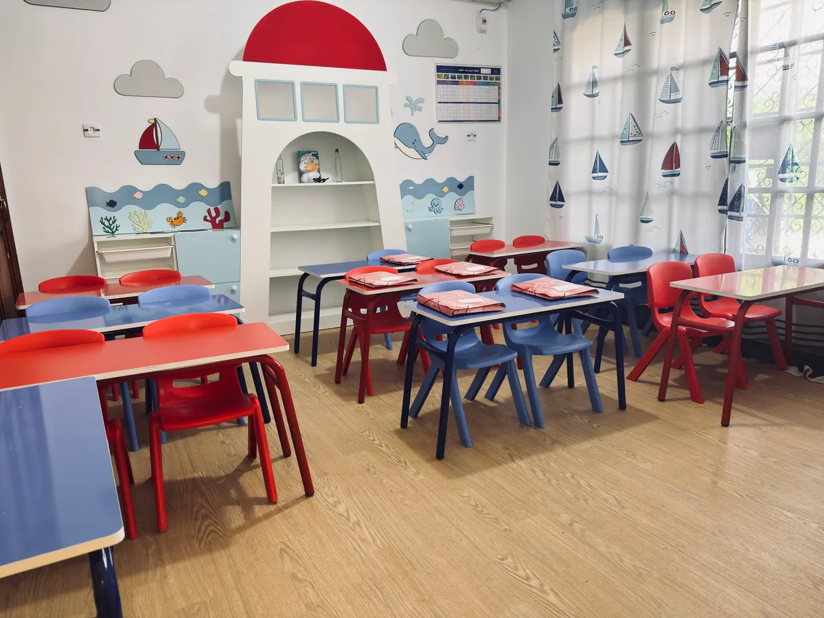 Sea-themed classroom: a lighthouse shelf, blue and red tables and sailboat curtains.